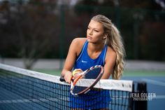 a woman holding a tennis racquet on top of a tennis court next to a net