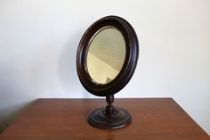 a mirror sitting on top of a wooden table next to a white wall with a brown base