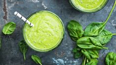 two glasses filled with green smoothie next to spinach leaves