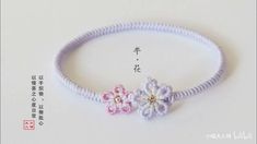 the bracelet has two flowers on it and is made from white string with pink and purple beads