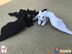 two stuffed animals laying on the ground next to each other, one black and one white dragon