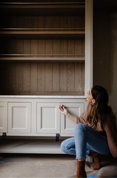 a woman sitting on the floor in front of a bookcase holding a paint roller