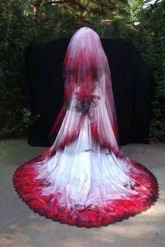 a woman in a white and red wedding dress standing on the ground with her veil draped over her head