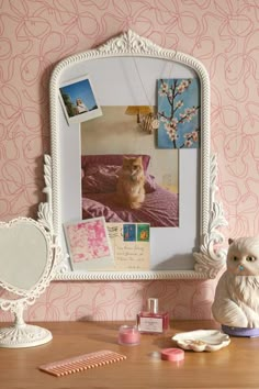 a desk with a mirror, figurine and other items on it in front of a pink wallpapered background