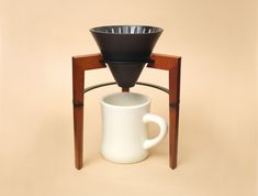 a white coffee cup sitting on top of a wooden stand next to a black cone