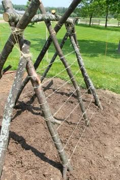 a wooden structure made out of sticks and rope in the middle of a dirt field