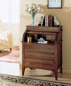 a small wooden cabinet sitting in the corner of a room next to a rug and vase with flowers