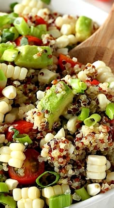 a white bowl filled with corn, tomatoes and green peppers next to a wooden spoon