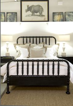 a black iron bed frame with white linens and pillows in a bedroom decorated with pictures on the wall