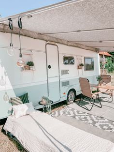 an rv is parked under a tent and has a table with chairs on it next to the camper