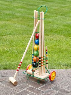 an outdoor game set made out of wooden sticks and balls on a brick walkway with grass in the background