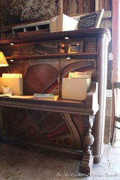 an old piano has been turned into a desk with many items on it and is sitting next to a lamp