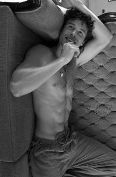 a shirtless man laying on a couch with his hand under his head and looking at the camera