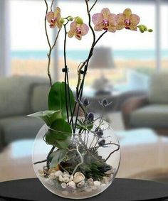 a glass vase filled with flowers and plants on top of a table next to a couch