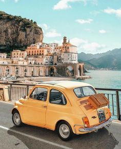 an orange car parked on the side of a road next to a body of water