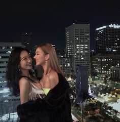 two beautiful women standing next to each other in front of a cityscape at night