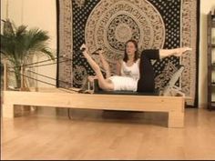 a woman sitting on top of a wooden bench in front of a wall hanging tapestry