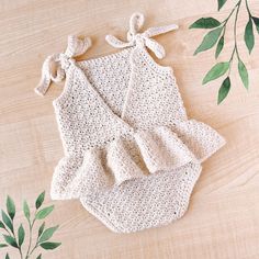 a crocheted baby dress and diaper cover on a wooden surface with green leaves