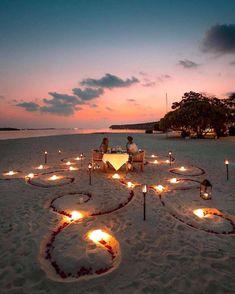 two people sitting at a table on the beach with candles in the shape of a heart