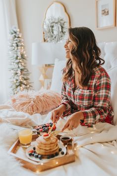 a woman sitting on top of a bed next to a tray filled with pancakes and berries