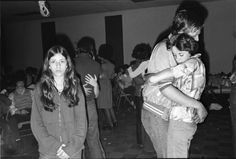 black and white photograph of people dancing in a room full of other people, some with their arms around each other