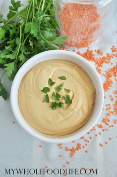 a white bowl filled with hummus next to carrots and parsley