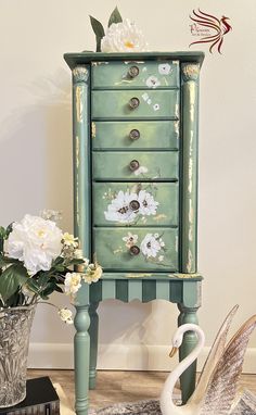 a green dresser with flowers on it next to a white swan