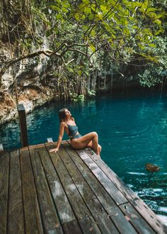 a woman sitting on top of a wooden dock next to a body of blue water