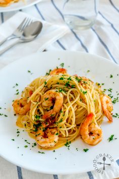 pasta with shrimp and parsley on a white plate next to a glass of water