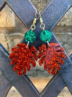 two red and green leaves are hanging from a pair of earrings