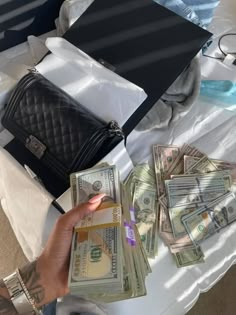 a person holding money in front of a purse on top of a white cloth covered table