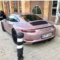 a pink car parked on the side of a street next to a black and white striped pole