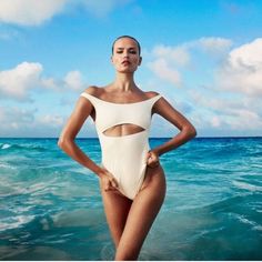 a woman standing in the ocean wearing a white one piece swimsuit with cutouts