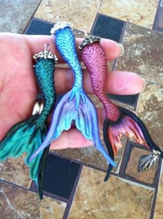 two mermaid tail shaped rings sitting on top of a person's hand in front of a tile floor