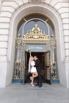 a man and woman are kissing in front of a city hall entrance with the doors open