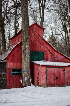 an old red barn sits in the snow next to a fence and trees with no leaves on it