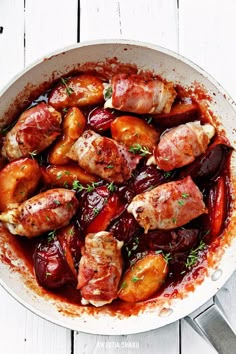 a pan filled with meat and vegetables on top of a white wooden table next to utensils