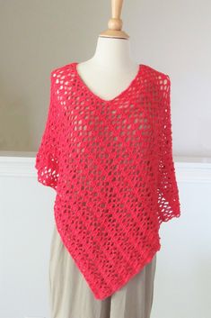 a woman wearing a red crocheted shawl on top of a mannequin