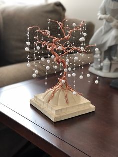 a sculpture of a tree with white balls on it sitting on a table in front of a couch