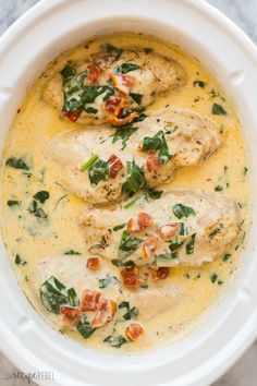 a white crock pot filled with chicken and spinach garnished in cream sauce