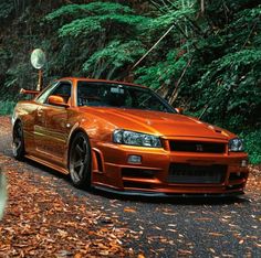 an orange sports car parked on the side of a road in front of some trees