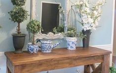 a wooden table topped with vases filled with flowers next to a mirror and potted plants