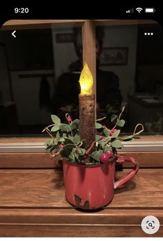 a lit candle in a red cup on a window sill with greenery and berries