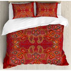 a bed with red and orange bedspread on top of wooden floor next to white pillows