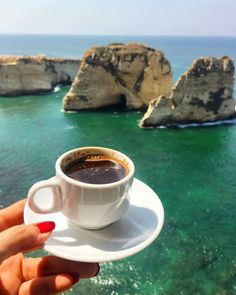 a cup of coffee sitting on top of a white saucer next to the ocean