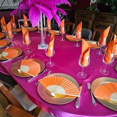 the table is set with orange and pink plates, silverware, and purple feather centerpieces