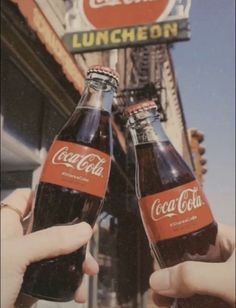 two people holding up beer bottles in front of a building