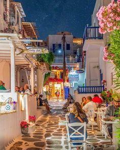 people are sitting at tables in an alleyway with flowers and potted plants on either side