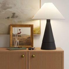 a lamp sitting on top of a wooden cabinet next to a painting and framed pictures