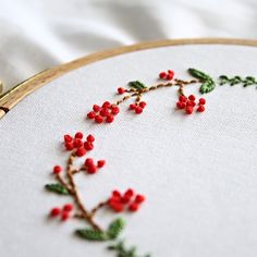 a close up of a embroidery on a white cloth with red berries and green leaves